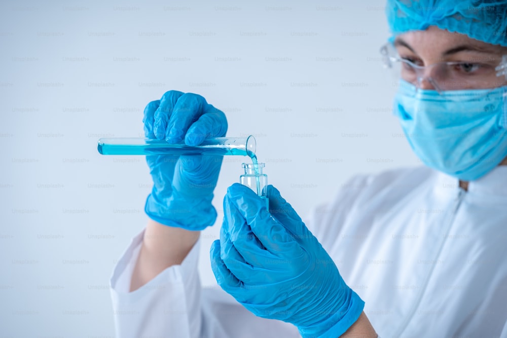 Health care development concept. Scientist woman in coat and protective gloves making laboratory research, holding test tube with blue fluid, mixing reagents, standing isolated on white background