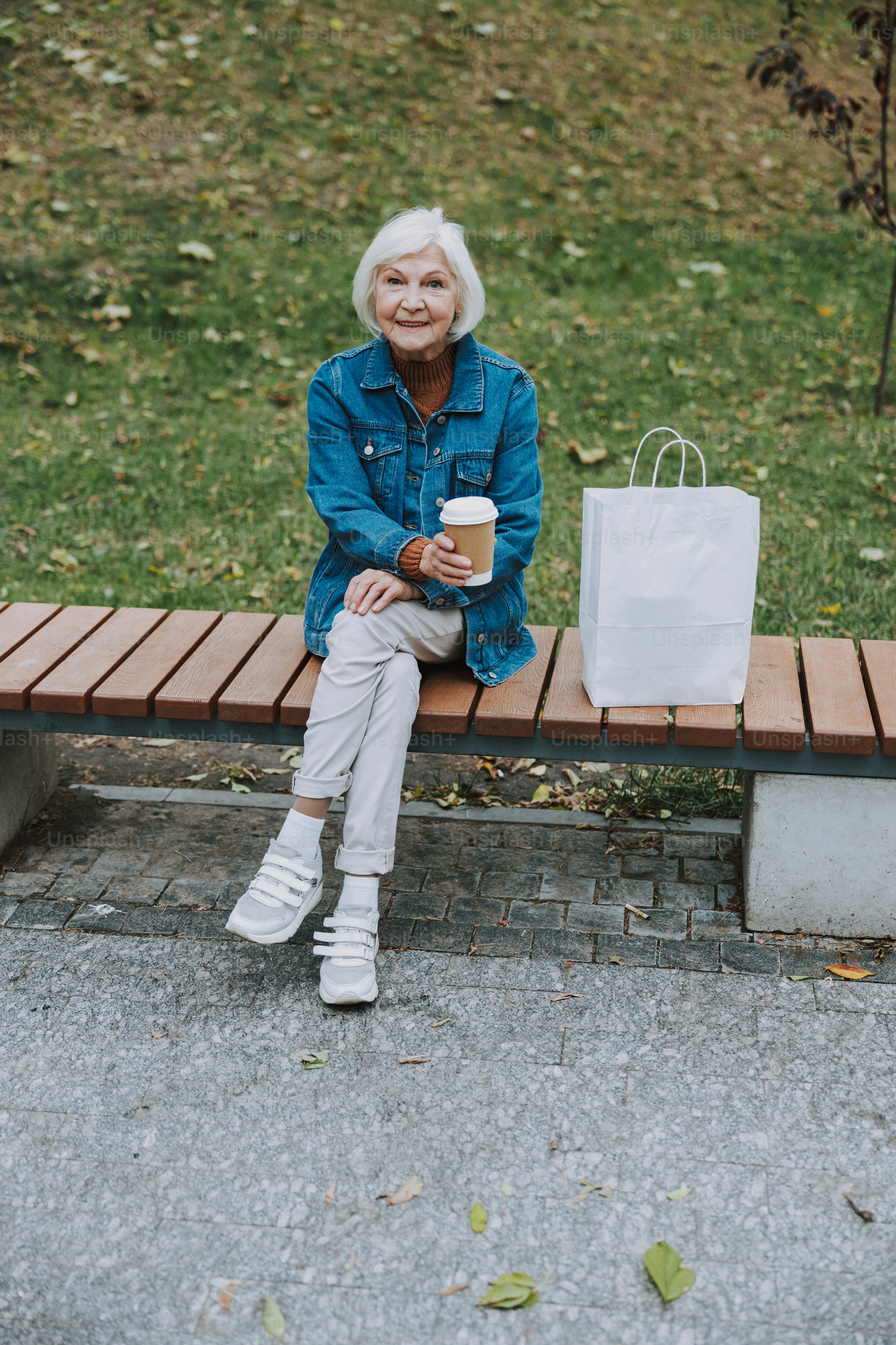 Mulher sorridente na jaqueta jeans que segura a bebida quente da foto de stock