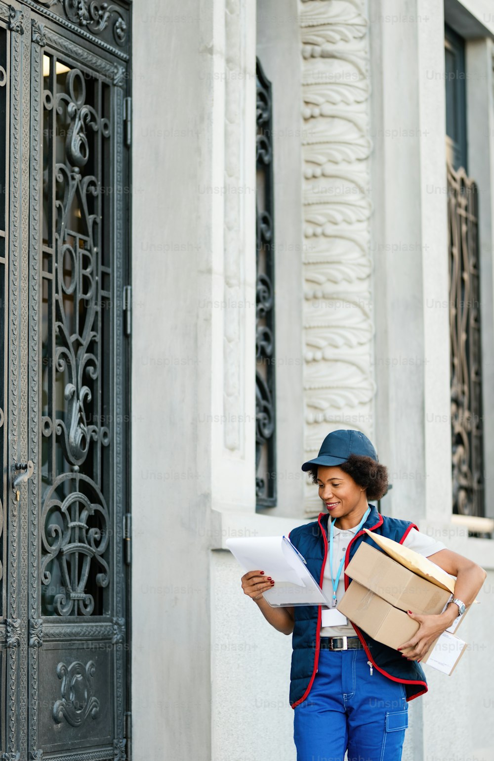 Mensajera afroamericana sonriente entregando paquetes mientras lee la dirección en la lista en la ciudad.