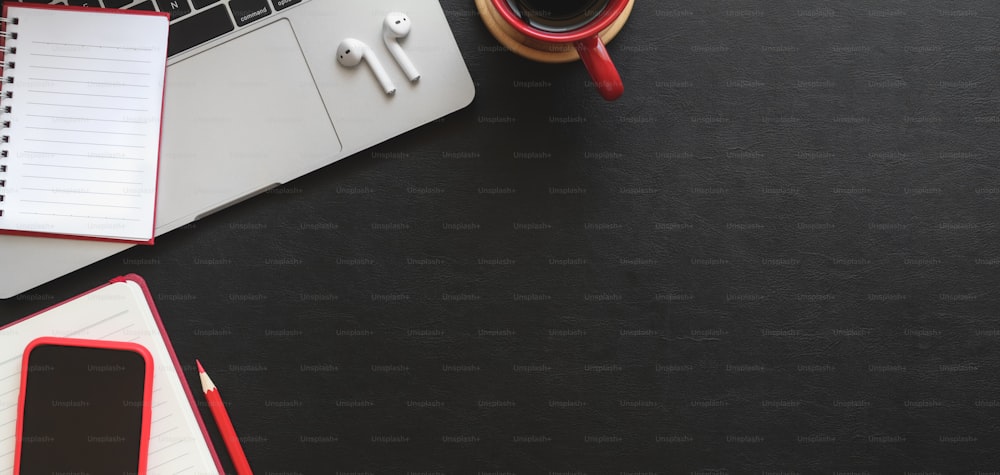 Top view of dark modern workplace with notebook, laptop computer and office supplies on black table background