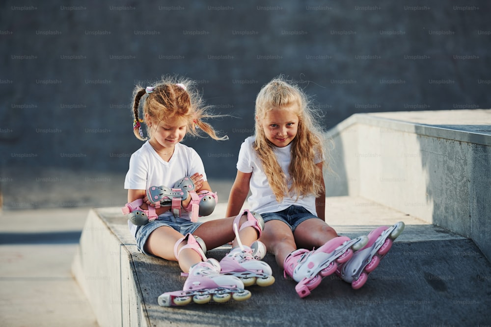 Having a rest. On the ramp for extreme sports. Two little girls with roller skates outdoors have fun.