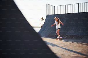 Sunny day. Kid have fun with skate at the ramp. Cheerful little girl.