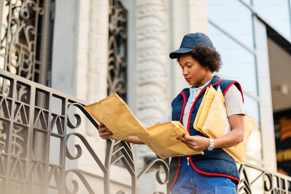 Black female courier making a delivery and reading address on a package.