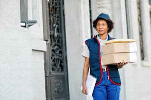Portrait of African American female deliverer with packages standing on the street and looking away.