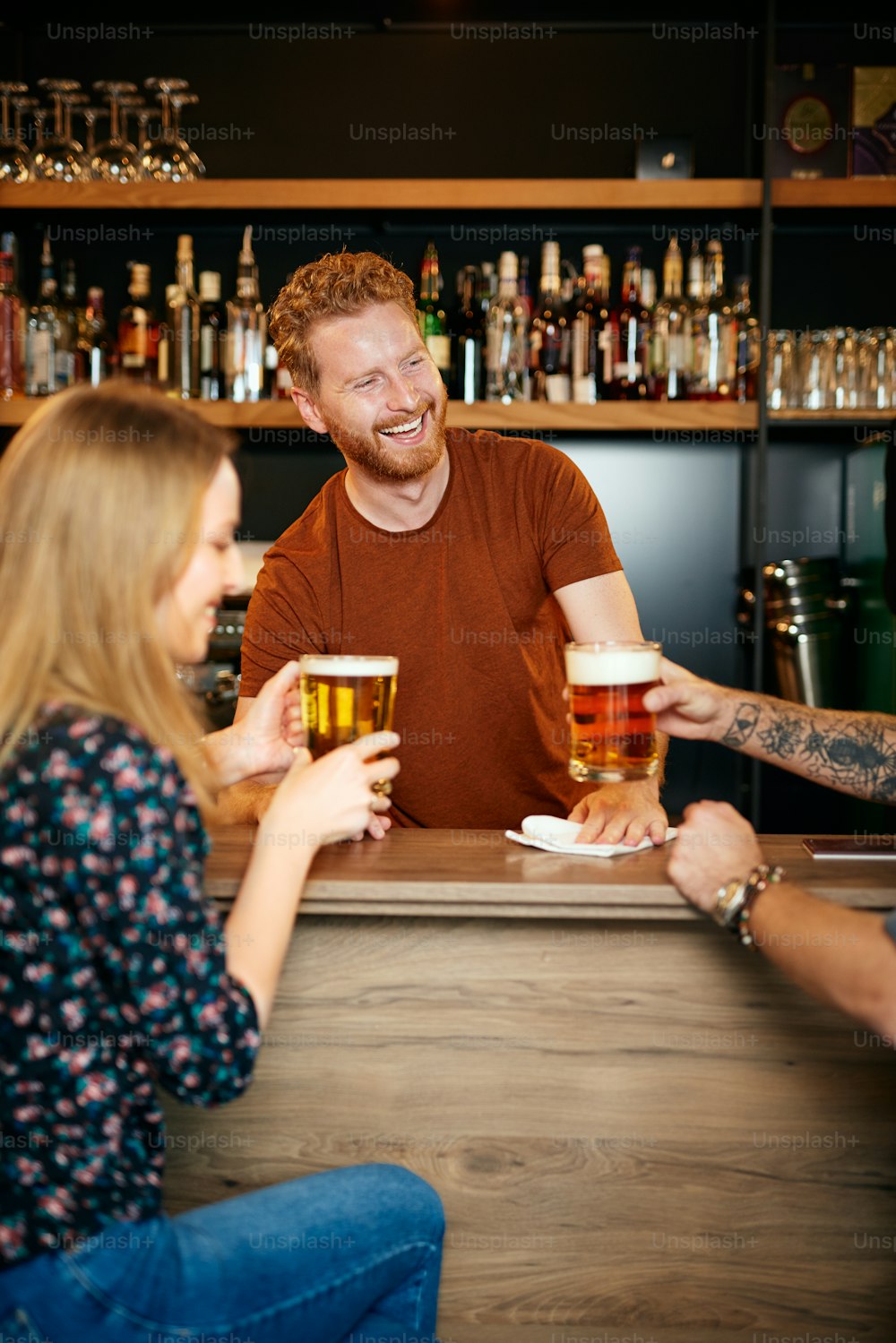 Amigos alegres apoyados en la barra del bar, bebiendo cerveza y charlando con el camarero. Salida nocturna.