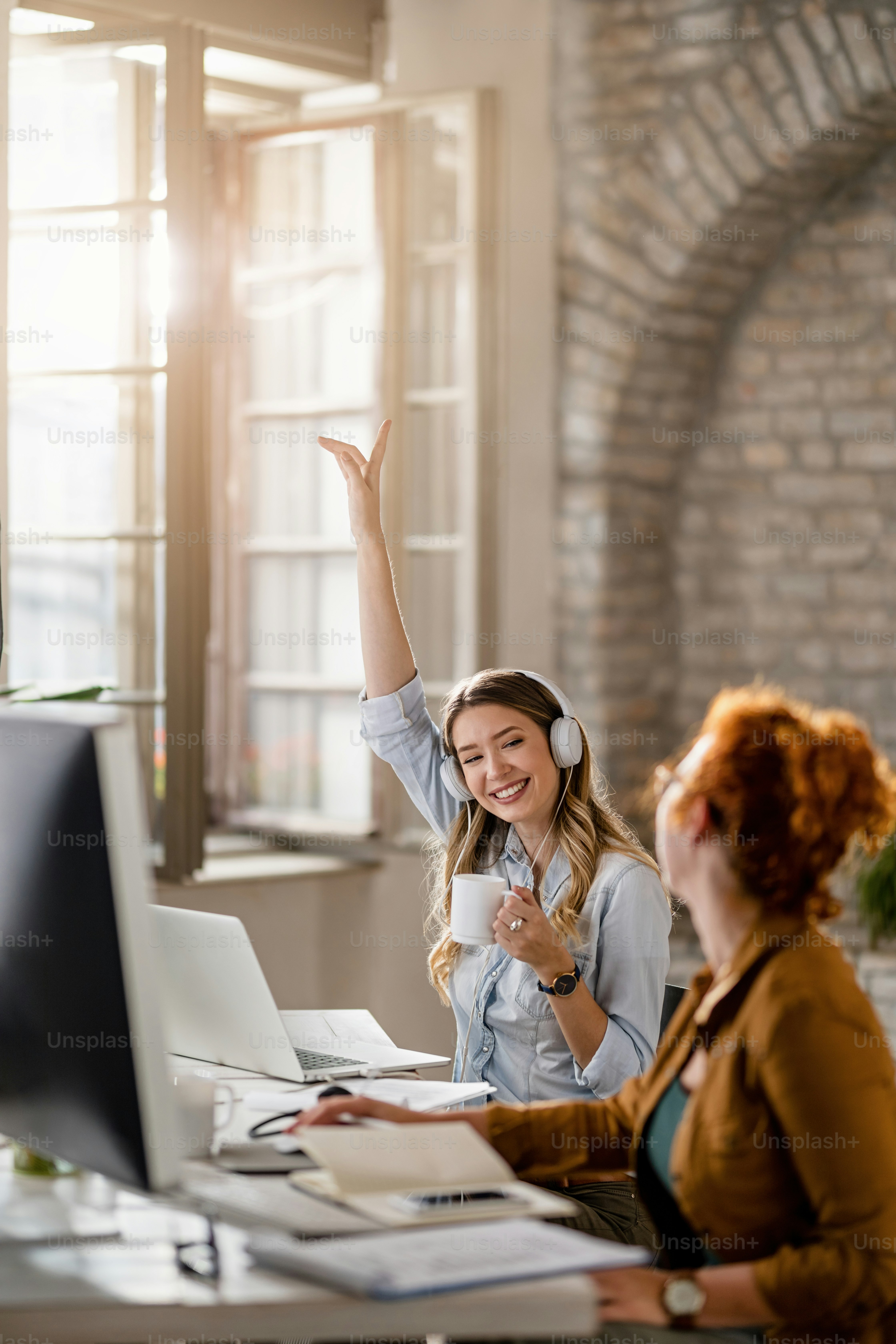 Feliz mujer de negocios con auriculares y divirtiéndose mientras escucha música y bebe café en la oficina.