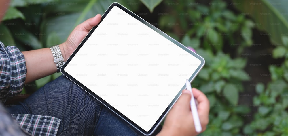 Foto cortada de empresário trabalhando em seu projeto com tablet de tela em branco com jardim ao fundo