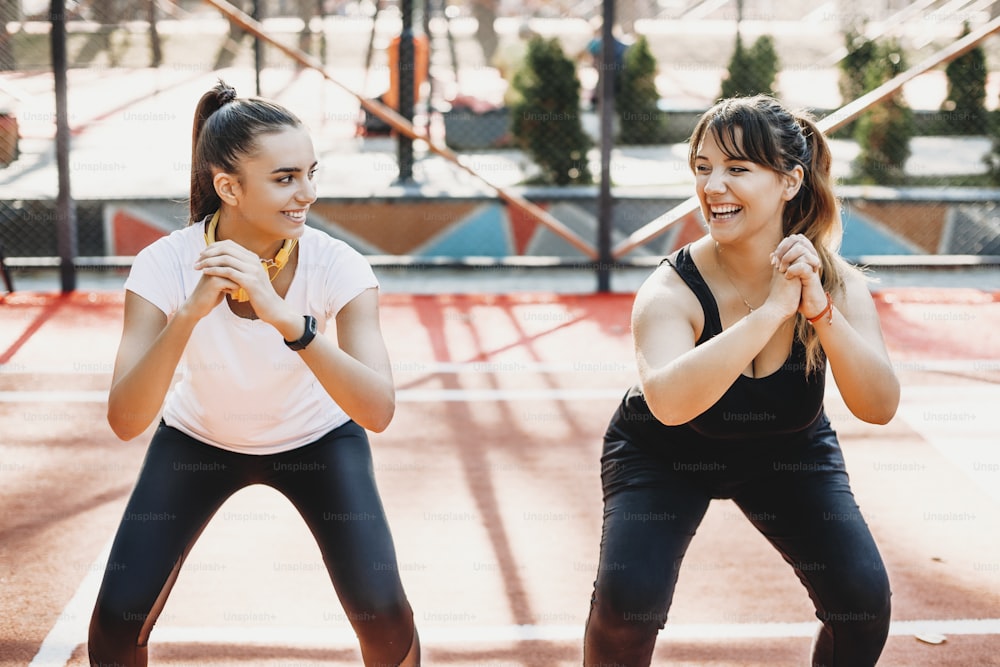 Portrait of a lovely young plus size women laughing while doing exercises for lose weight with her girlfriend in a sport park.