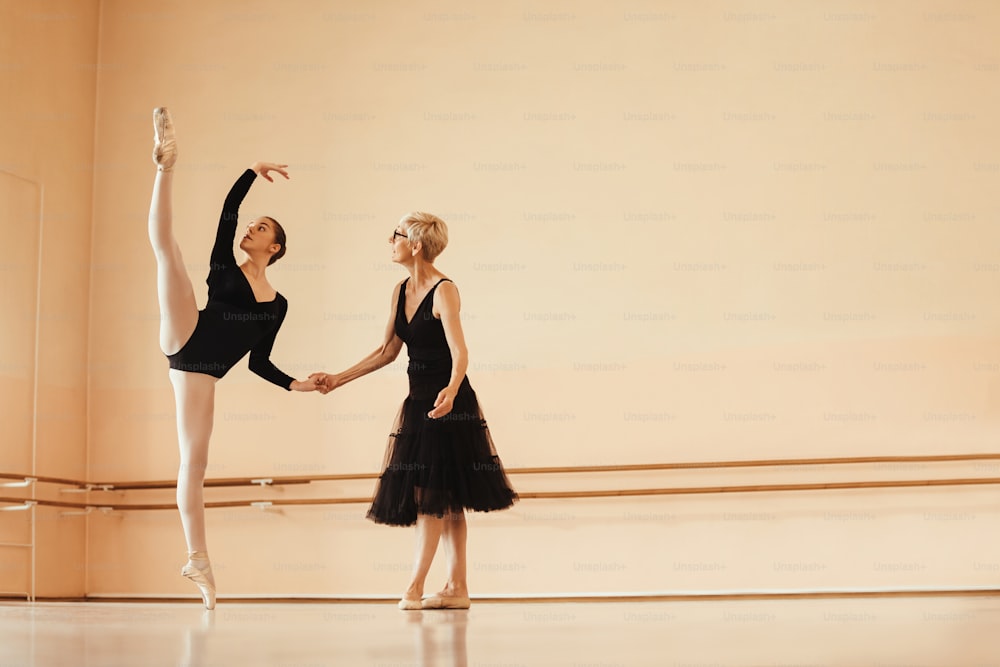 ダンススタジオでのリハーサル中の成熟したバレエインストラクターと若いバレリーナのフルレングス。スペースをコピーします。