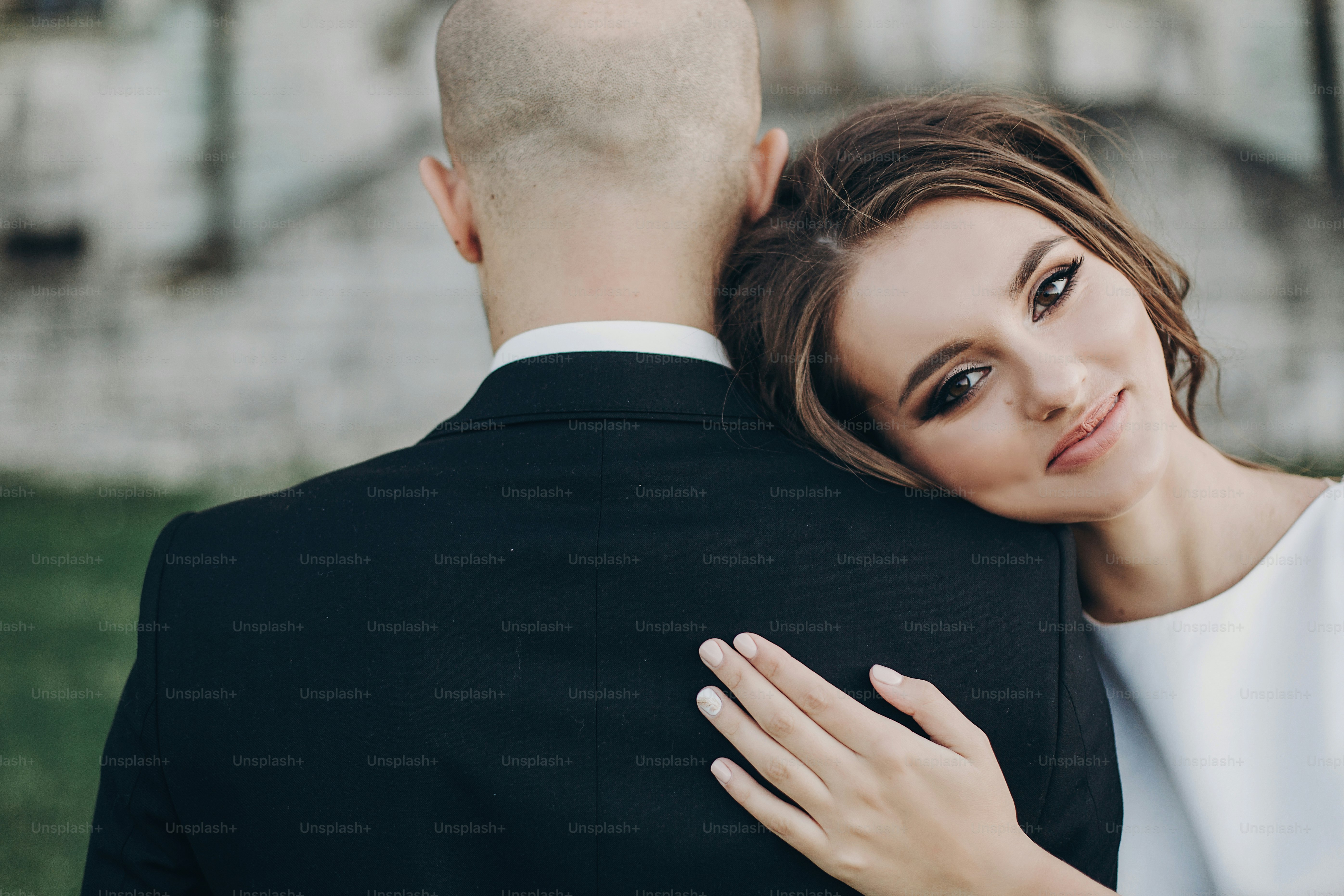 Gorgeous bride and groom embracing in evening sunlight near old castle in park. Romantic moment. Stylish wedding couple gently hugging and smiling