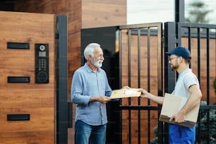 Joven trabajador postal que hace entregas a domicilio y entrega un paquete a un cliente mayor en la puerta principal.