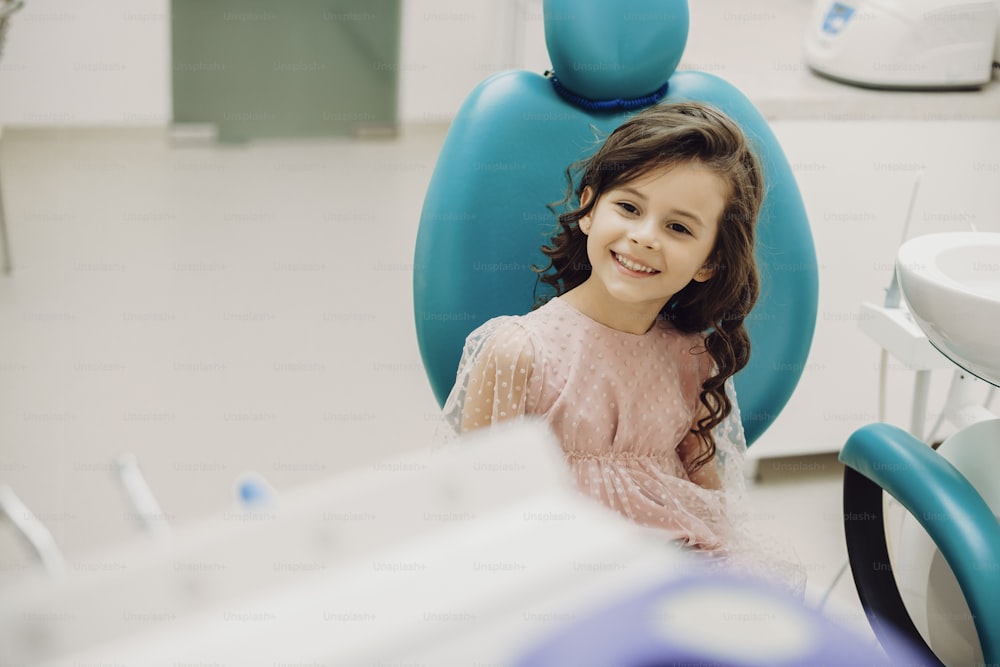 Belle petite fille riant assise dans un siège de stomatologie avant de faire un examen des dents dans une stomatologie pédiatrique.