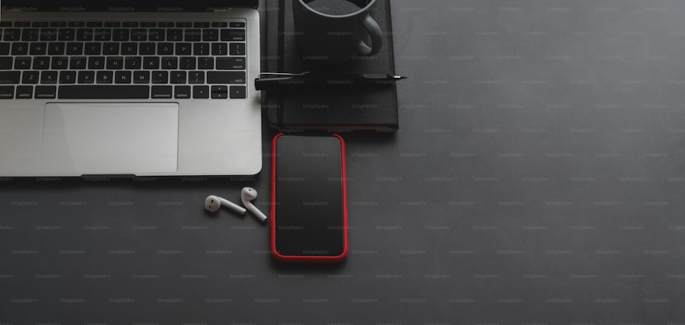 Overhead-Aufnahme von Laptop und Smartphone mit Kopierplatz auf schwarzem Tischhintergrund