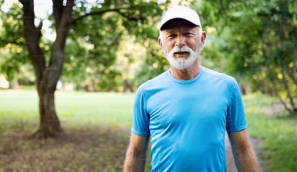 Séduisant homme âgé à la retraite avec un beau sourire faisant du jogging dans le parc