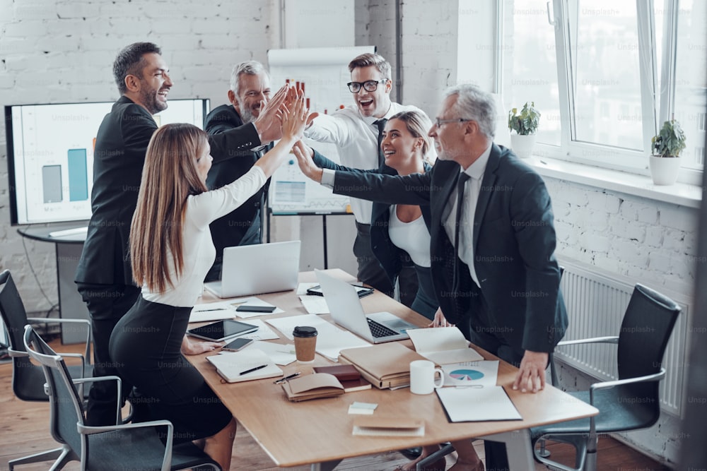 Equipe de negócios alegre dando uns aos outros cinco altos para o sucesso enquanto trabalham no escritório moderno