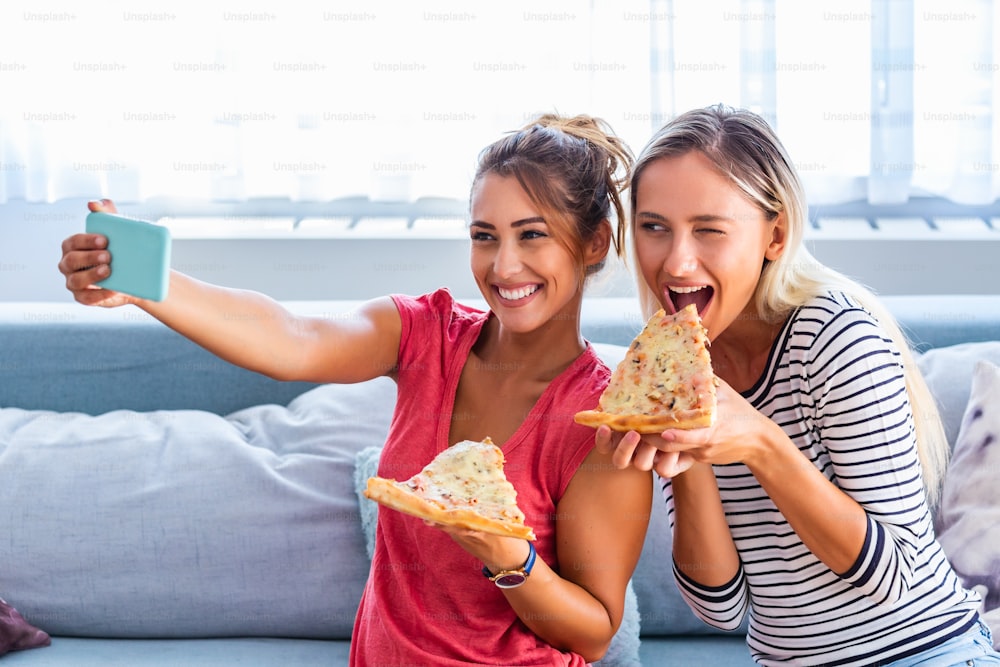Freunde essen Pizza und lächeln für Selfies. Sie teilen Pizza und machen Selfie-Fotos auf dem mobilen Smartphone. Sie feiern zu Hause, essen Pizza und haben Spaß.
