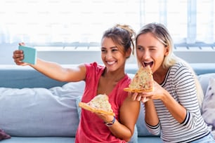 ピザを食べたり、笑顔で自撮りしたりする友達。彼らはピザを共有し、モバイルスマートフォンで自撮り写真を作っています。彼らは家でパーティーをしたり、ピザを食べたり、楽しんでいます。
