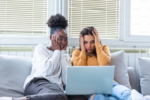 Frightened young women watching movie at home. Girls watching a terror movie on tv sitting on a couch at home. Girlfriends watching scary movie on laptop at home