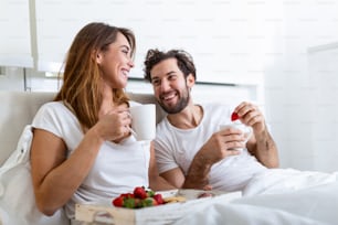 Young married couple in love eating breakfast in their bed. Good morning! Healthy breakfast in bed. Young beautiful love couple is having breakfast in bed.