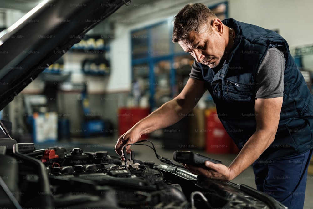 Automechaniker mit Diagnosewerkzeug bei der Überprüfung der Spannung der Autobatterie in einer Werkstatt.