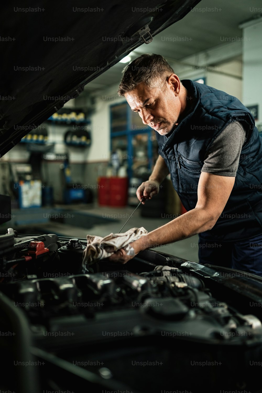 自動車修理工場で作業しながら、自動車エンジンのオイルをチェックする自動車整備士。