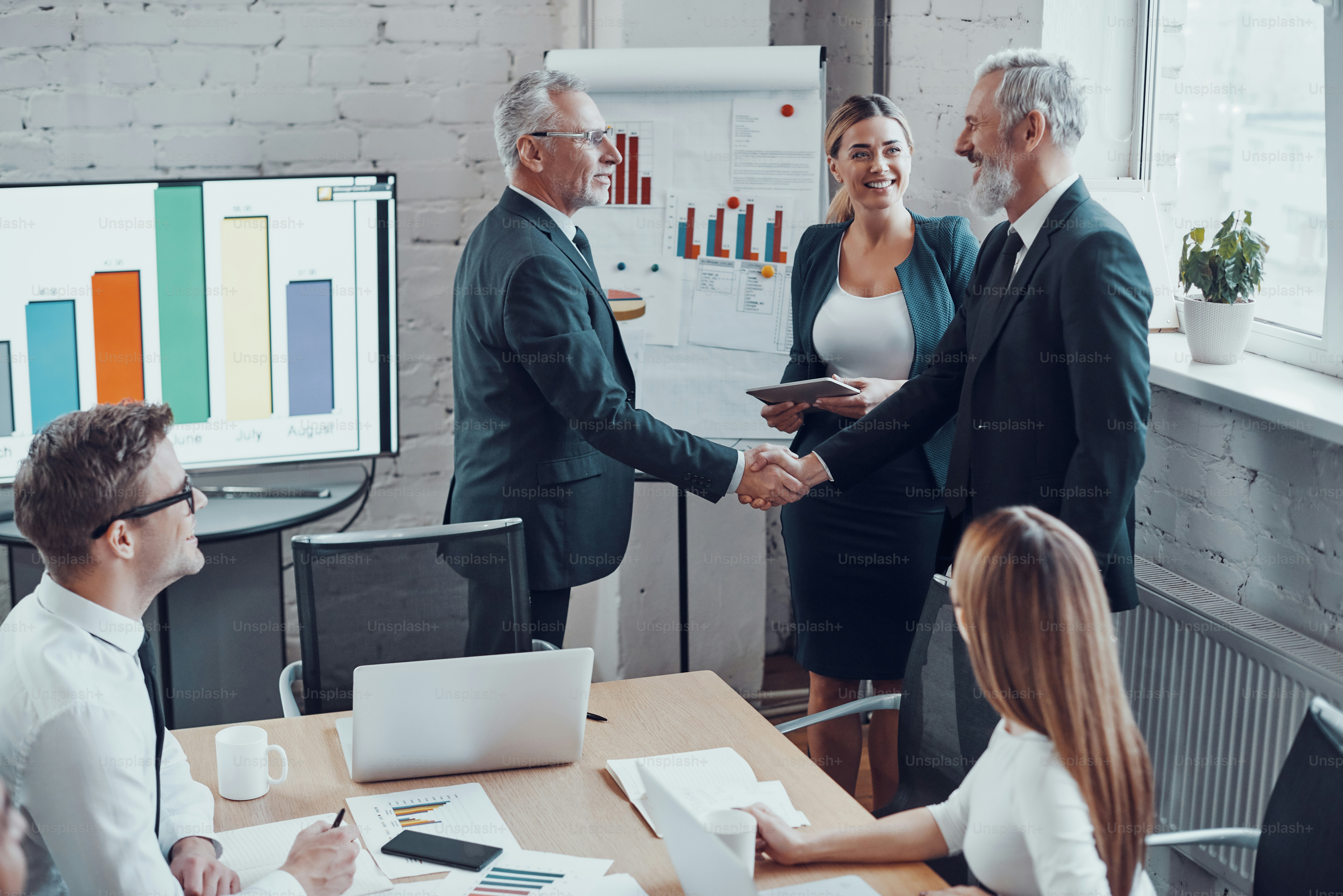Confident businessmen shaking hands and smiling while working together with colleagues in the board room