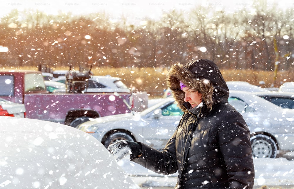Young woman brushing the snow off in snowfall his car in a cold winter day