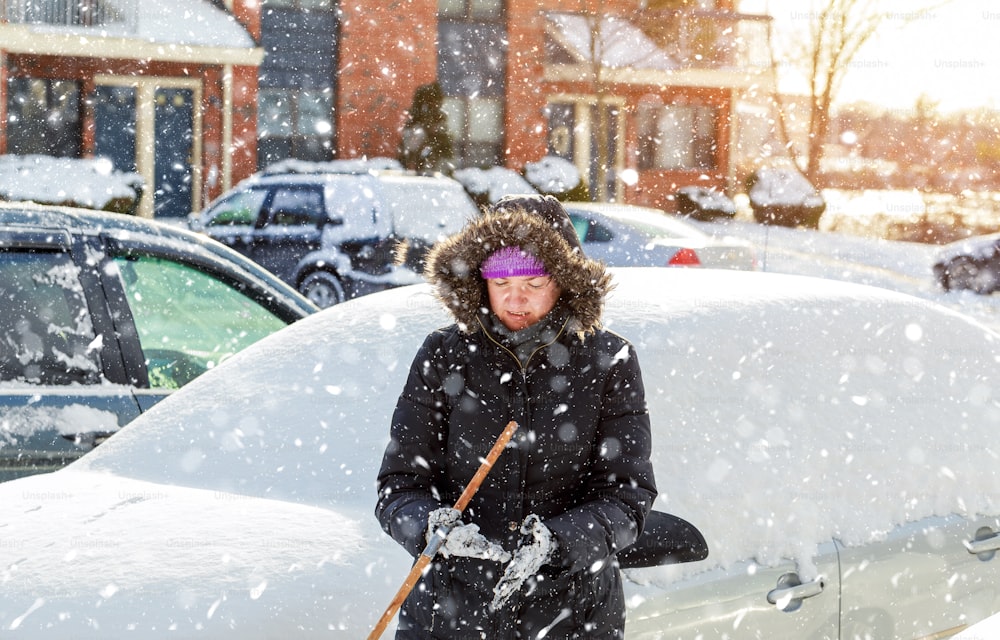 Donna che pulisce l'auto da neve usando la spazzola in inverno mattina