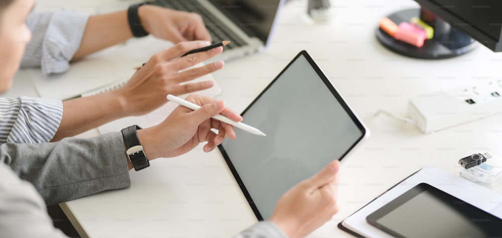 Cropped shot of young professional UX web developer team working on their project together with tablet