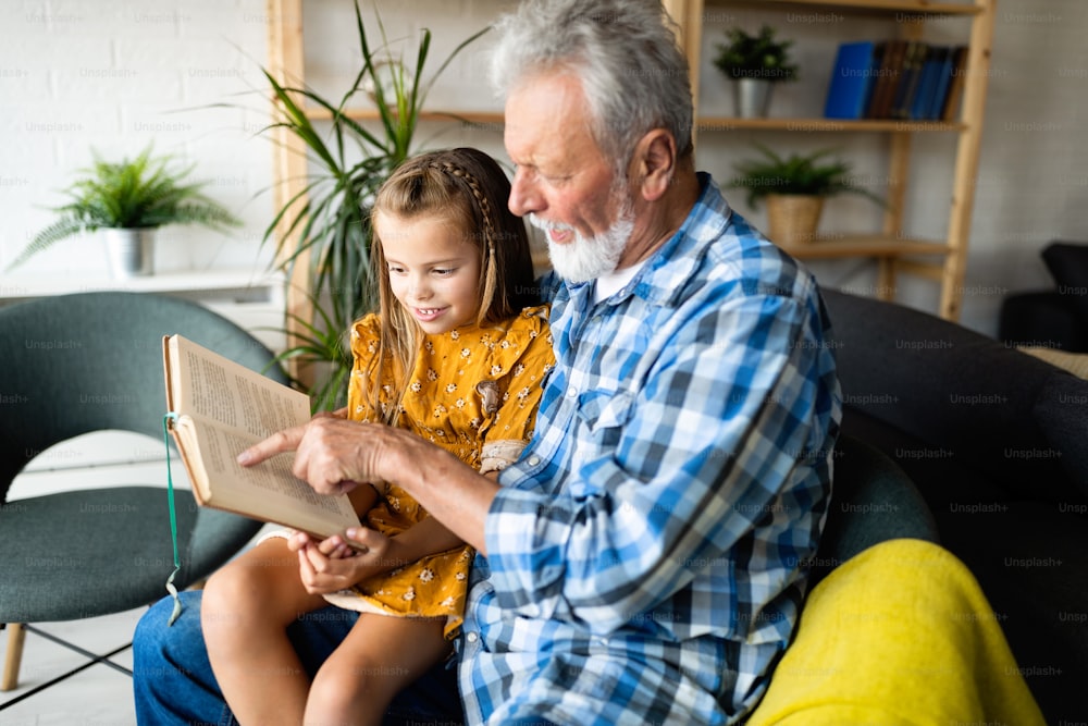 Bearded aged grandfather and his grandchild are having fun reading a book together