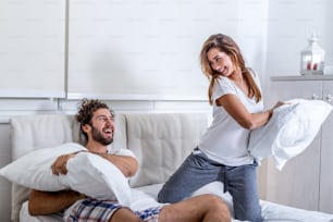 Happy young couple is having fun in bed. Enjoying the company of each other. Pillow battle Funny couple fighting with pillows in bed