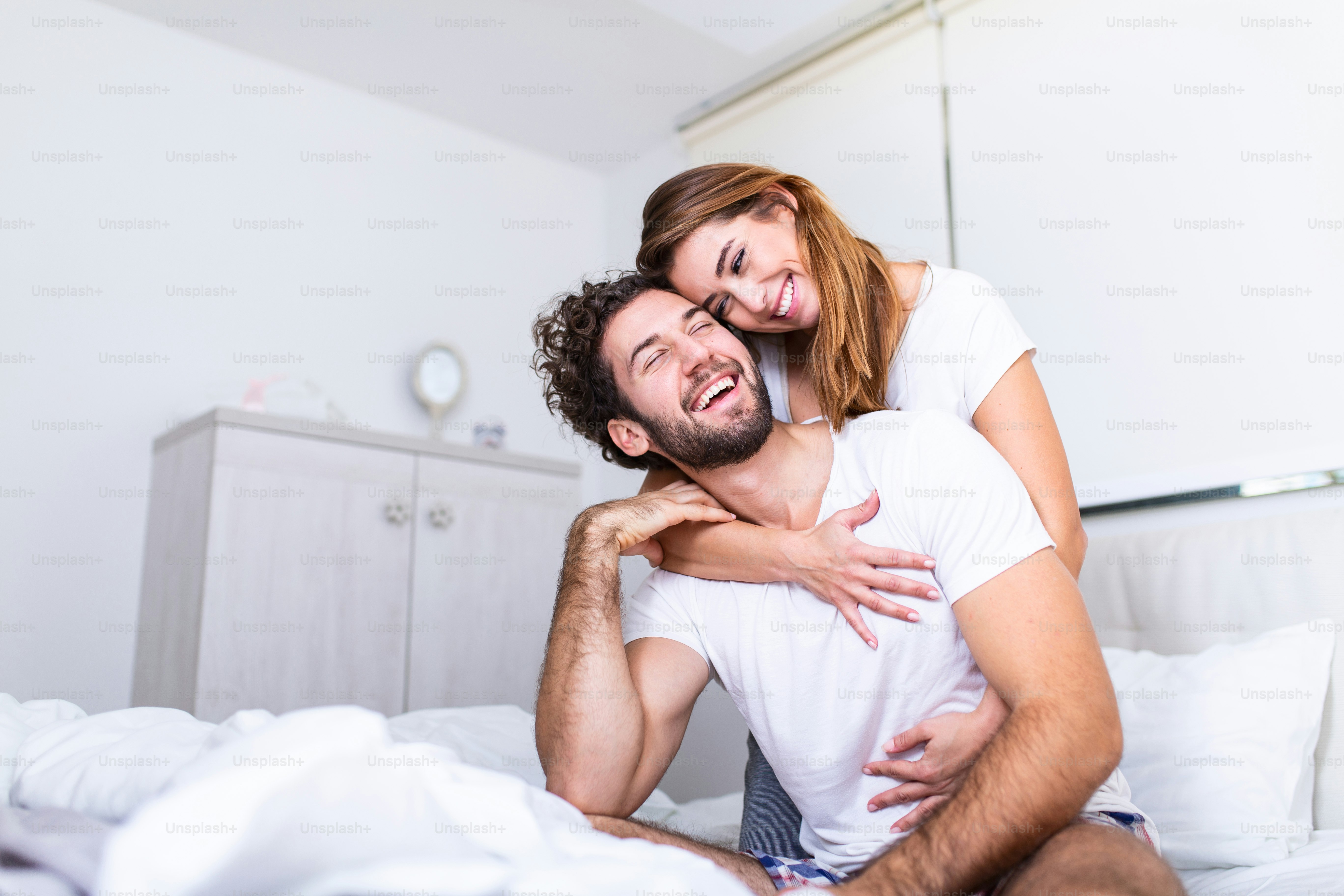 Woman embracing her partner in bed, Happy couple in bed showing emotions  and love. Beautiful loving couple kissing in bed. beautiful young couple  lying together on the bed. photo – Husband and