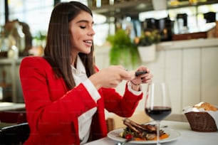 Attractive businesswoman in suit sitting in restaurant and taking picture of food over smart phone.