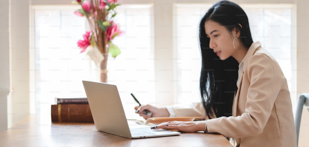Portrait d’une jeune belle femme d’affaires travaillant sur son projet avec un ordinateur portable dans un bureau confortable