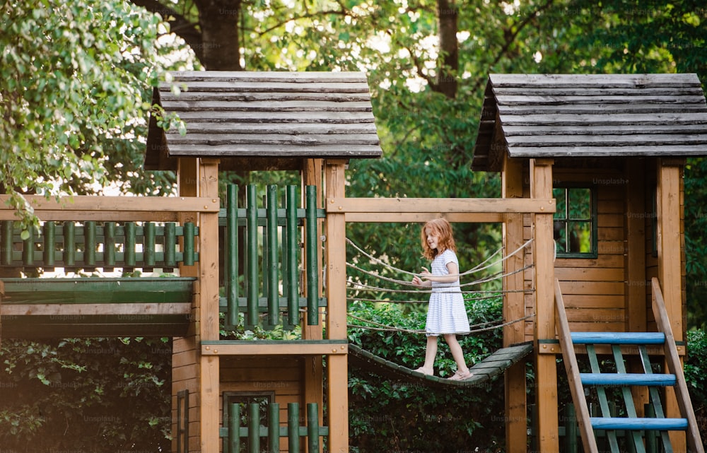 Una niña pequeña al aire libre en un patio de madera en el jardín en verano, jugando.