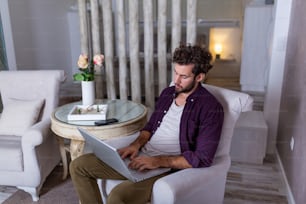 Serious bussines man with serious face sitting at home and using laptop for his project. freelance working from home concept Business man at home checking statistics on mobile phone and laptop