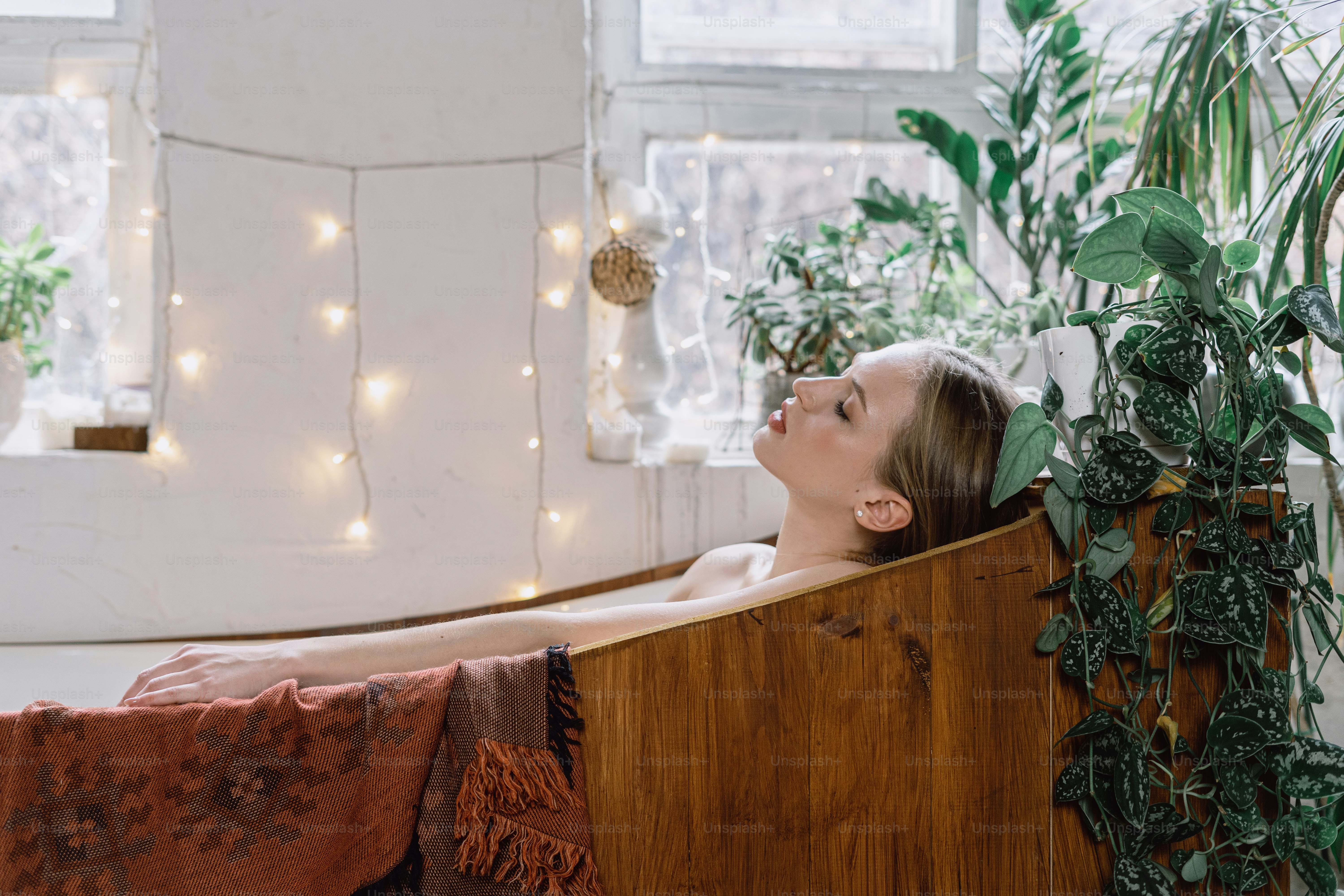 Side view of dreamy young adult woman lying in bathtub with closed eyes, resting at home, enjoying spa procedure