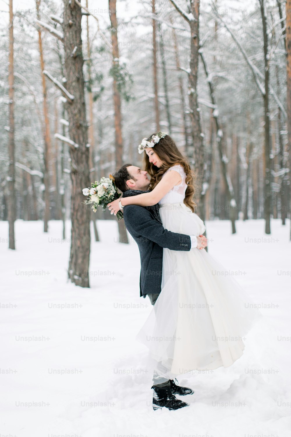 pretty young bride in wreath on the head kissing her handsome groom, a winter fairy tale. Winter wedding in the forest