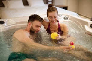 He enjoys making her laugh. Young couple in hot tub.