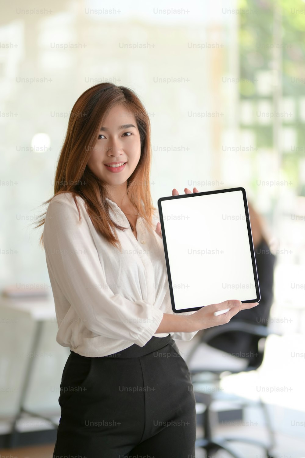 Portrait of young beautiful business woman showing blank screen digital tablet while standing in office room