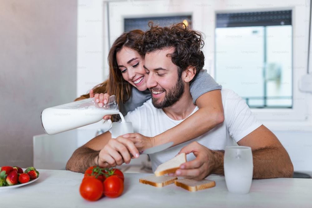 Portrait of happy young couple cooking together in the kitchen at home. Cute young couple enjoying their breakfast together she is pouring him milk wile