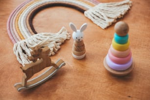 Stilvolles Holzspielzeug für Kinder auf Holztisch. Moderne bunte Holzpyramide mit Ringen, Holzhase und Makramee-Regenbogen. Umweltfreundliches plastikfreies Spielzeug für Kleinkinder