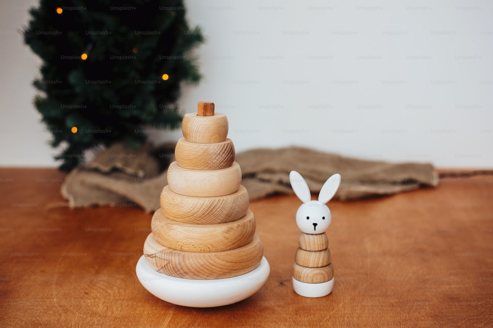 Stylish wooden toys for child on background of christmas tree. Modern simple wooden pyramid with rings and bunny. Eco friendly, plastic free educational toys for toddler