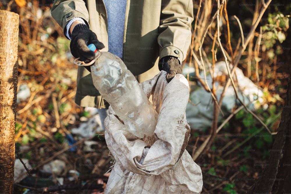 Un bénévole ramasse des bouteilles en plastique sales dans le parc. Femme main dans le gant ramassant les ordures, ramassant les ordures dans le sac. Nettoyer la nature avec du plastique à usage unique