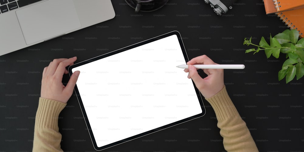 Top view of young woman working on her project with blank screen tablet and office supplies