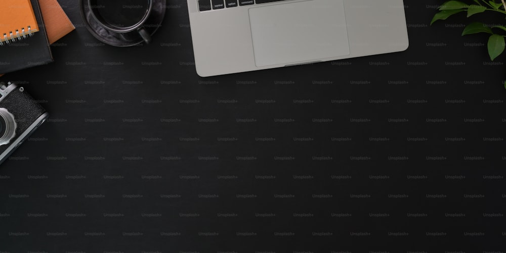 Tiro cenital de un lugar de trabajo oscuro y elegante con computadora portátil y suministros de oficina sobre fondo de mesa negro