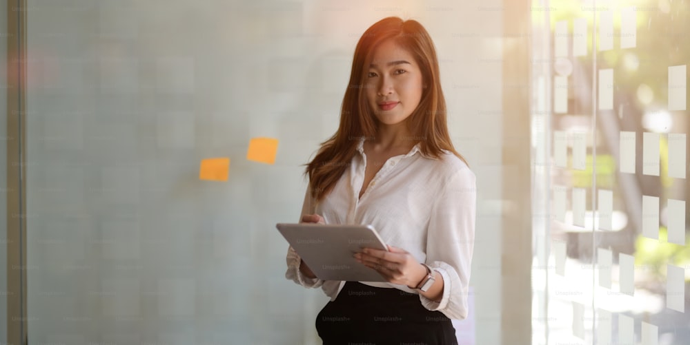 Portrait of beautiful businesswoman holding tablet while looking at the camera in modern workplace