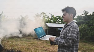 Concepto de tecnología agrícola, hombre con computadora portátil de pie en el campo agrícola.