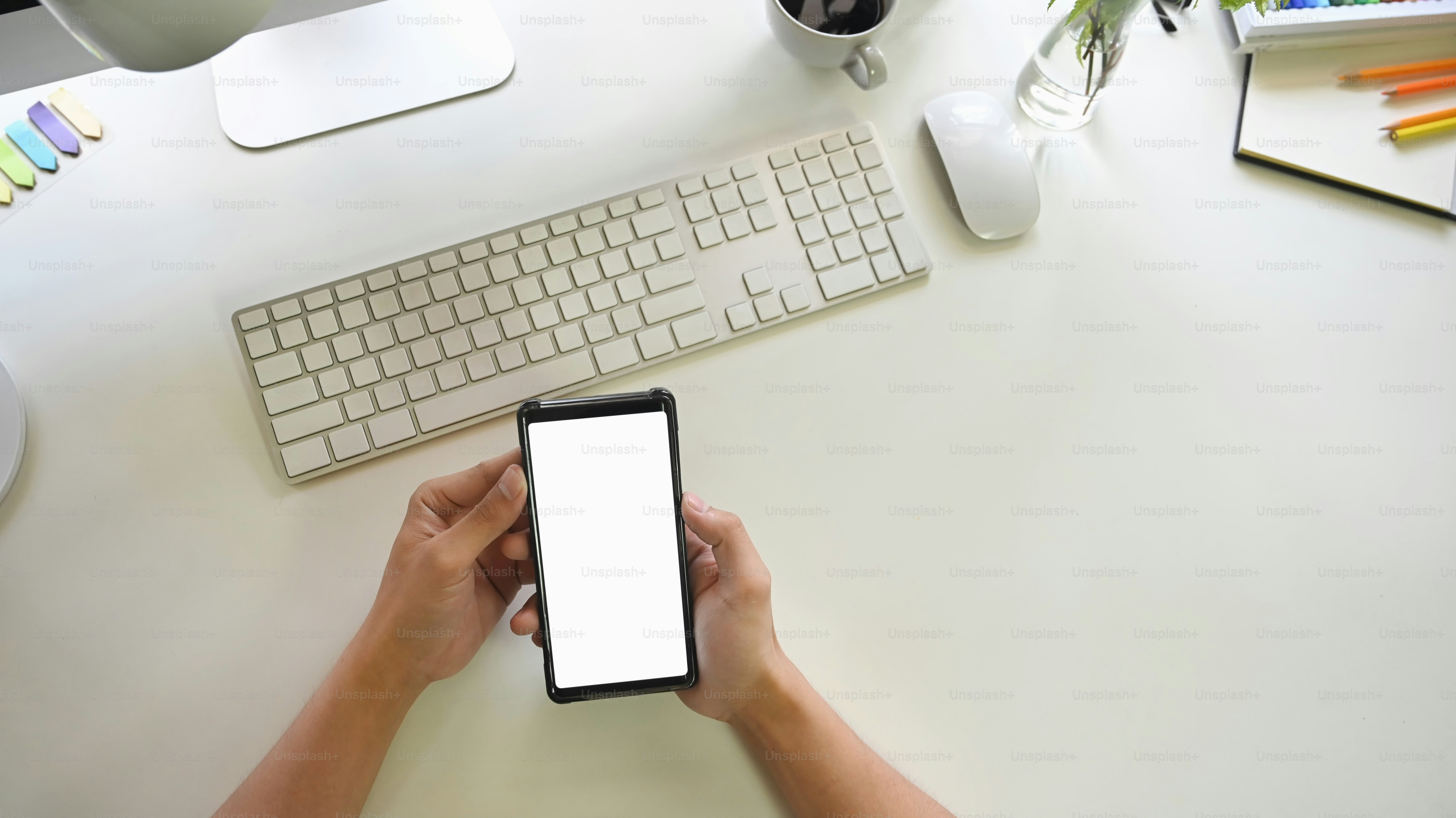 Man's hand holding white screen mobile phone on creative table.