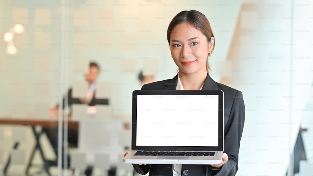 Businesswoman in suit showing isolated laptop computer front of meeting room.